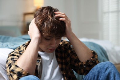 Photo of Teen problems. Depressed teenage boy near bed at home
