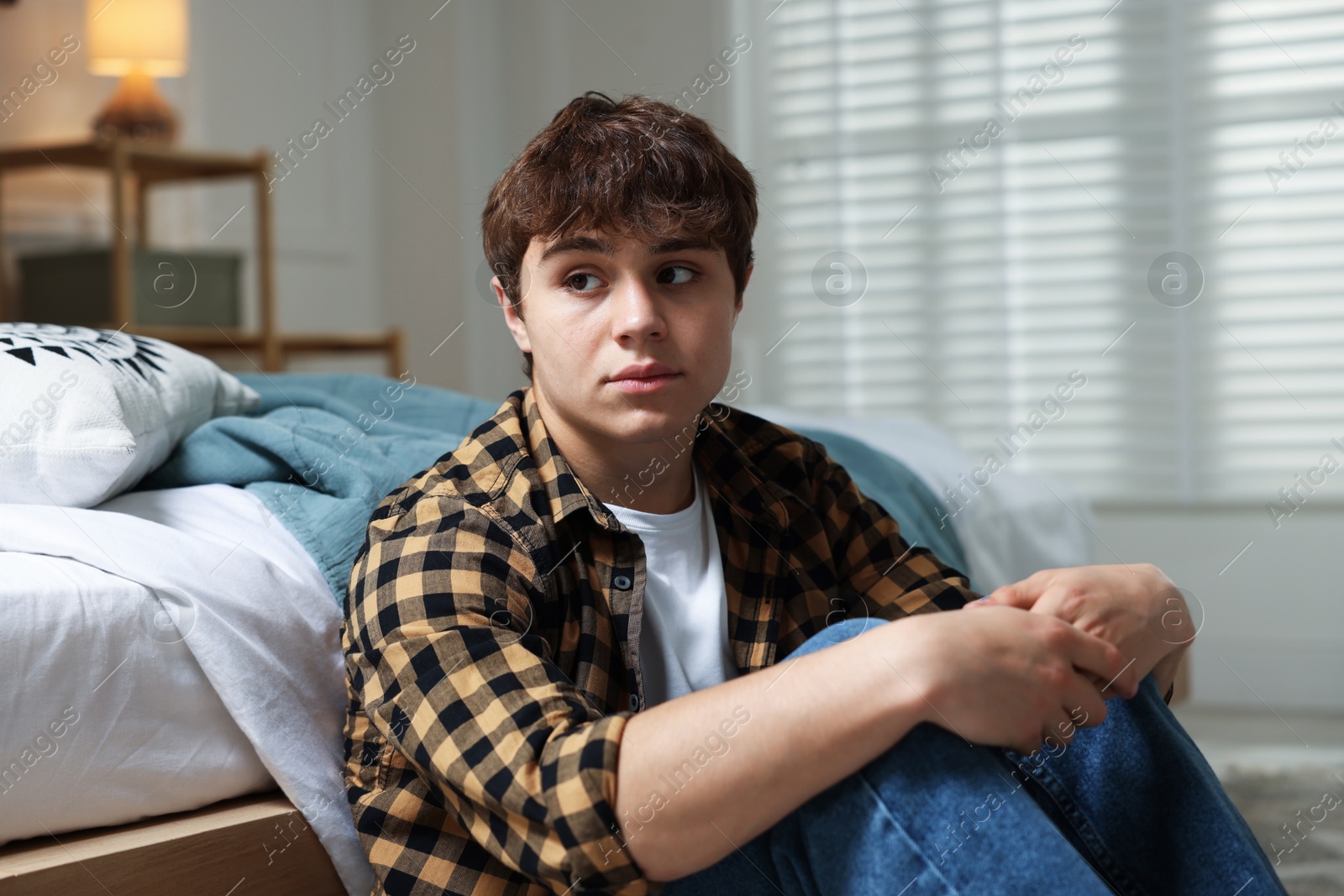 Teen problems. Upset teenage boy near bed at home Photo of Teen problems. Upset teenage boy near bed at home