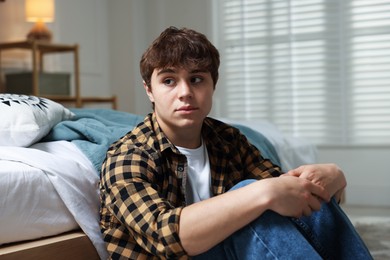 Photo of Teen problems. Upset teenage boy near bed at home