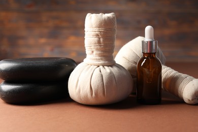 Photo of Massage bags, stones and cosmetic product on dark beige table, closeup. Spa composition