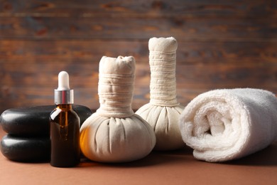 Photo of Massage bags, stones, towel and cosmetic product on dark beige table, closeup. Spa composition