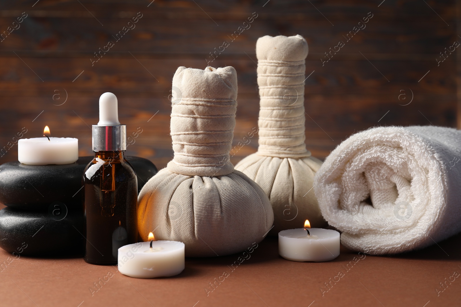 Massage bags, stones, towel, cosmetic product and burning candles on dark beige table, closeup. Spa composition Photo of Massage bags, stones, towel, cosmetic product and burning candles on dark beige table, closeup. Spa composition