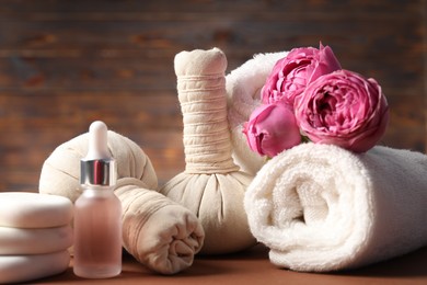 Photo of Massage bags, stones, towels, cosmetic product and peony flowers on dark beige table, closeup. Spa composition