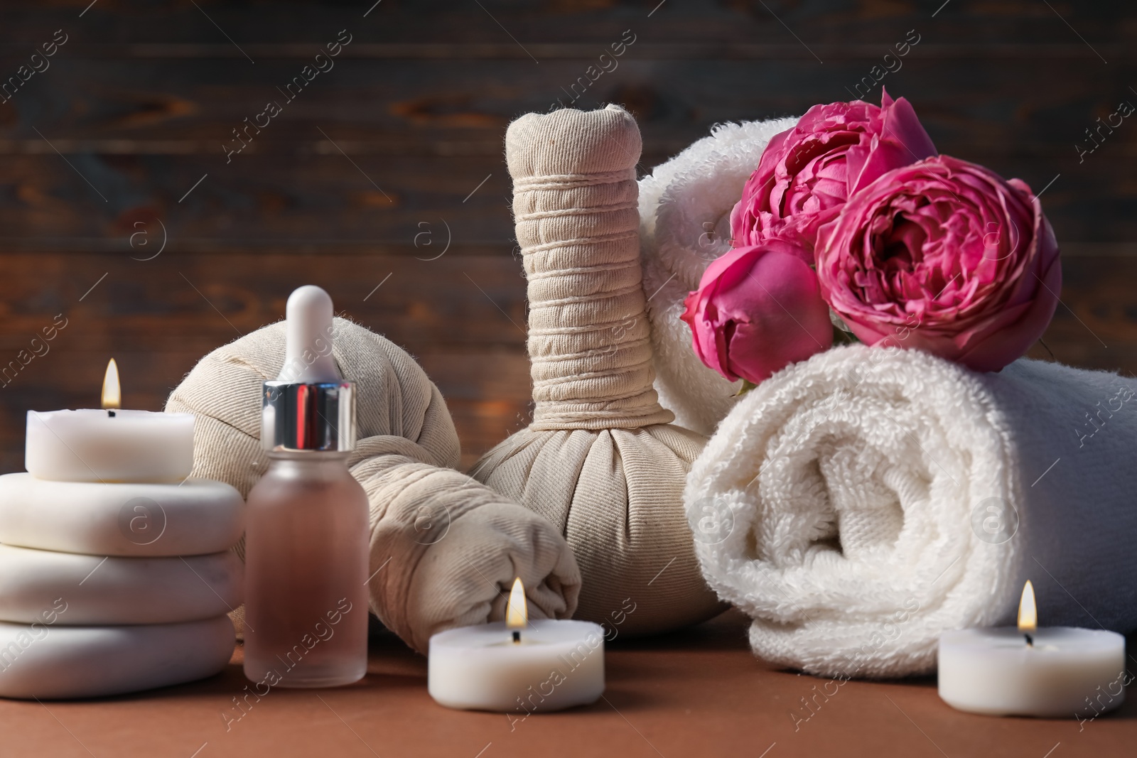 Massage bags, stones, towels, cosmetic product, peony flowers and burning candles on dark beige table, closeup. Spa composition Photo of Massage bags, stones, towels, cosmetic product, peony flowers and burning candles on dark beige table, closeup. Spa composition