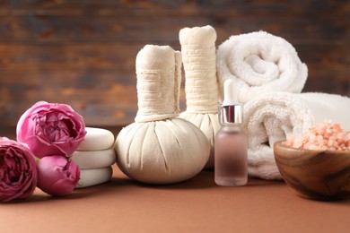 Photo of Massage bags, stones, towels, cosmetic products and peony flowers on dark beige table. Spa composition