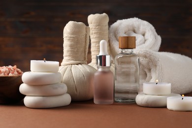 Photo of Massage bags, stones, towels, cosmetic products and burning candles on dark beige table. Spa composition