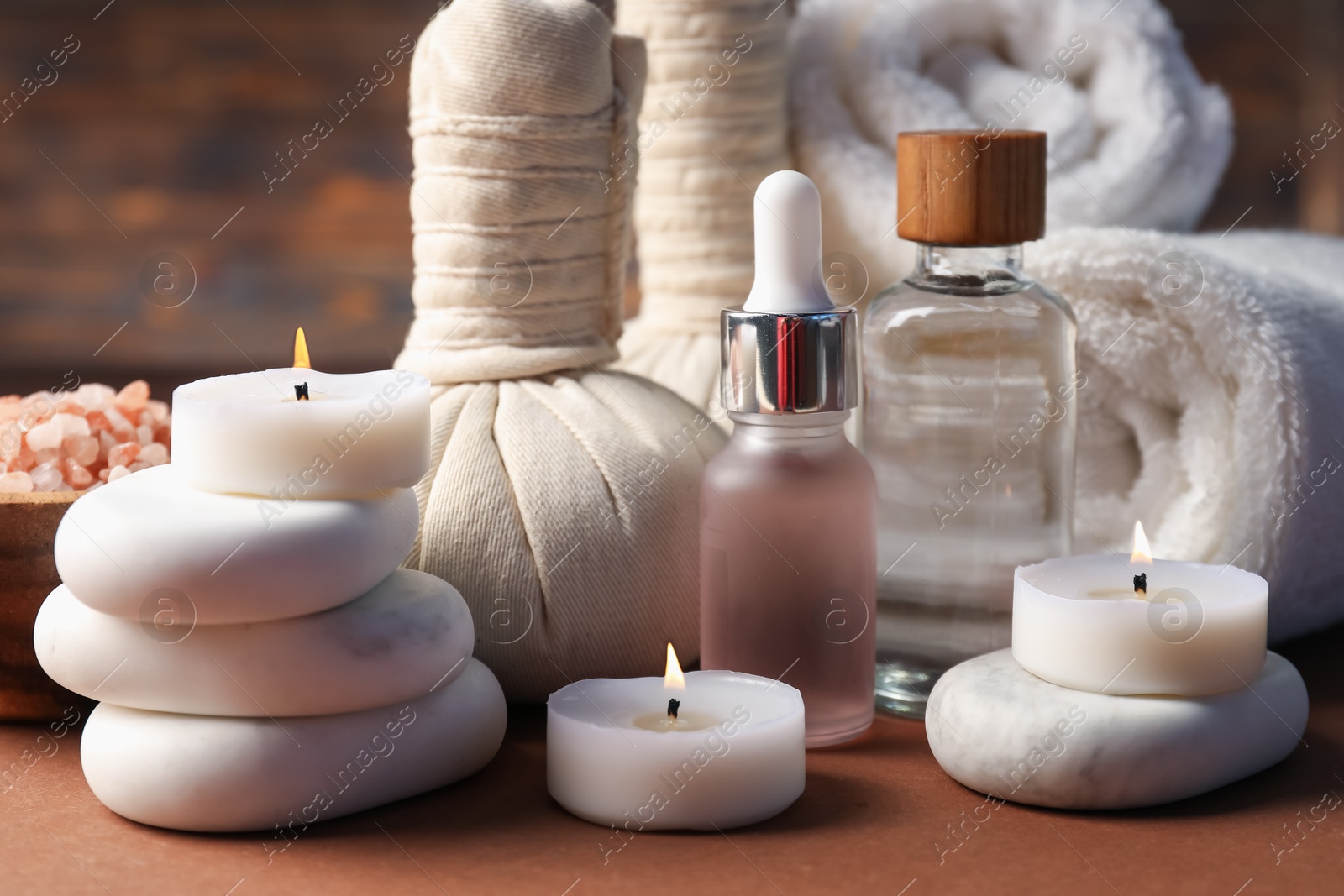 Massage bags, stones, towels, cosmetic products and burning candles on dark beige table, closeup. Spa composition Photo of Massage bags, stones, towels, cosmetic products and burning candles on dark beige table, closeup. Spa composition
