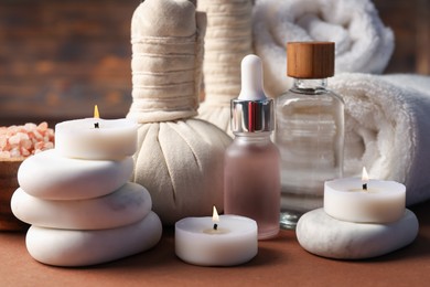 Photo of Massage bags, stones, towels, cosmetic products and burning candles on dark beige table, closeup. Spa composition