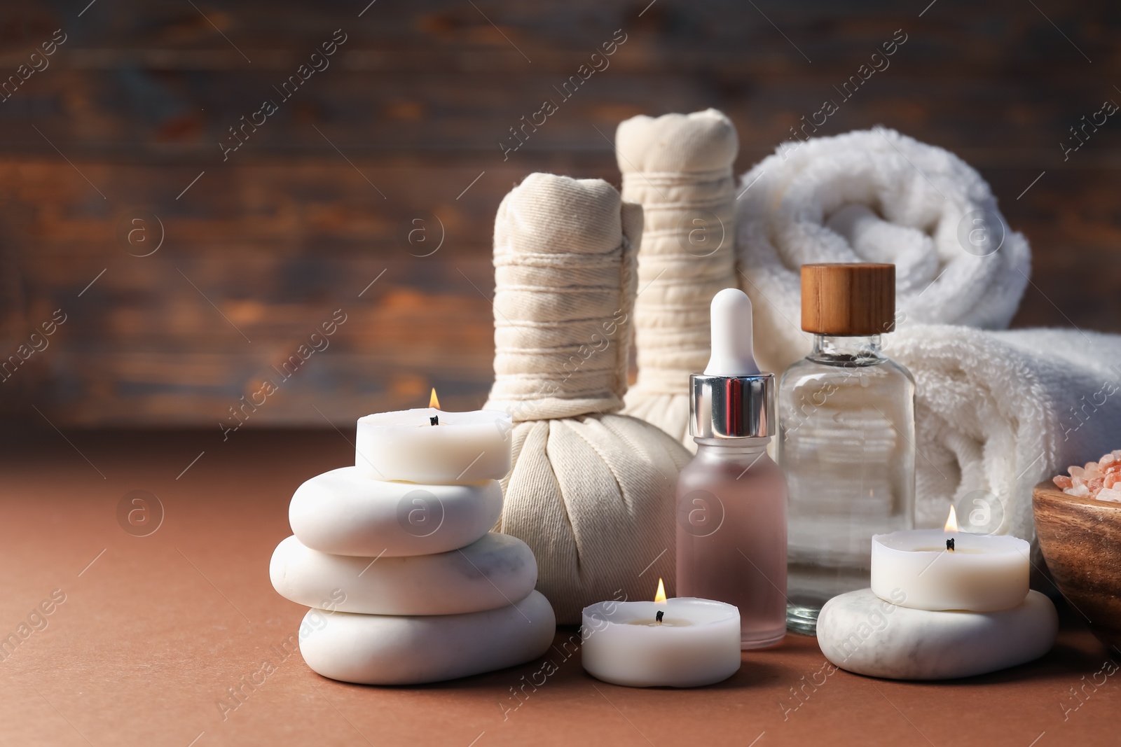 Spa composition. Massage bags, stones, towels, cosmetic products and burning candles on dark beige table, closeup. Space for text Photo of Spa composition. Massage bags, stones, towels, cosmetic products and burning candles on dark beige table, closeup. Space for text