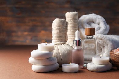 Photo of Spa composition. Massage bags, stones, towels, cosmetic products and burning candles on dark beige table, closeup. Space for text
