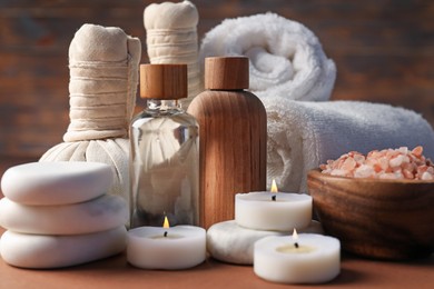 Photo of Massage bags, stones, towels, cosmetic products and burning candles on dark beige table, closeup. Spa composition