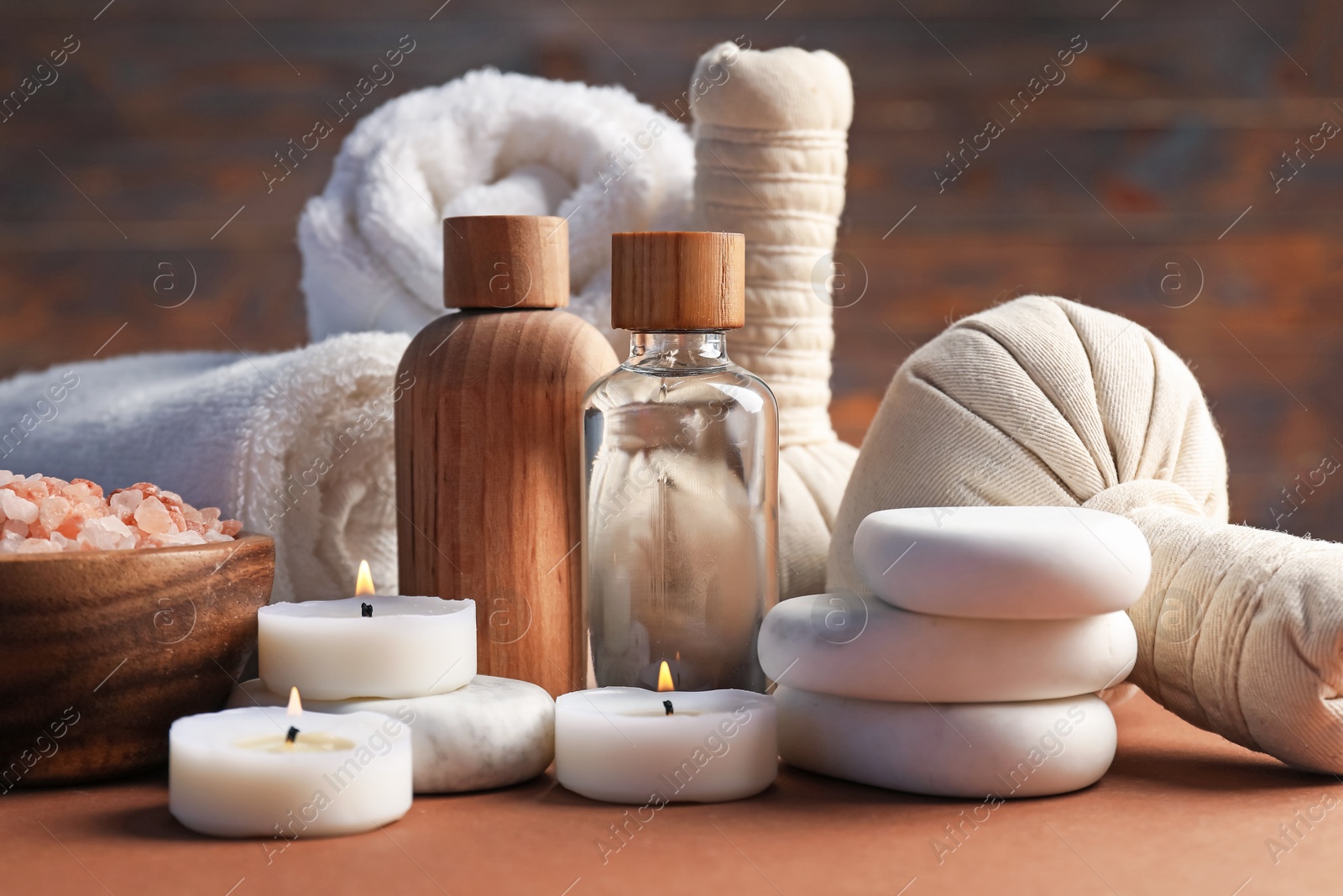 Massage bags, stones, towels, cosmetic products and burning candles on dark beige table, closeup. Spa composition Photo of Massage bags, stones, towels, cosmetic products and burning candles on dark beige table, closeup. Spa composition