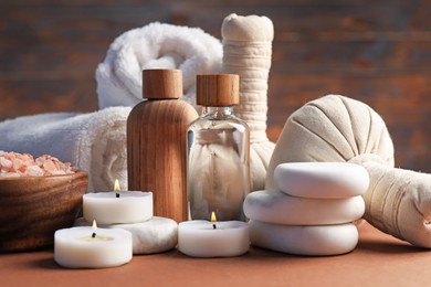 Photo of Massage bags, stones, towels, cosmetic products and burning candles on dark beige table, closeup. Spa composition
