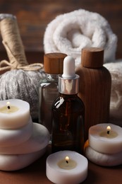 Photo of Massage bag, stones, towels, cosmetic products and burning candles on dark beige table, closeup. Spa composition