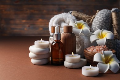 Photo of Spa composition. Massage bags, stones, towels, cosmetic products, plumeria flowers and burning candles on dark beige table, closeup. Space for text