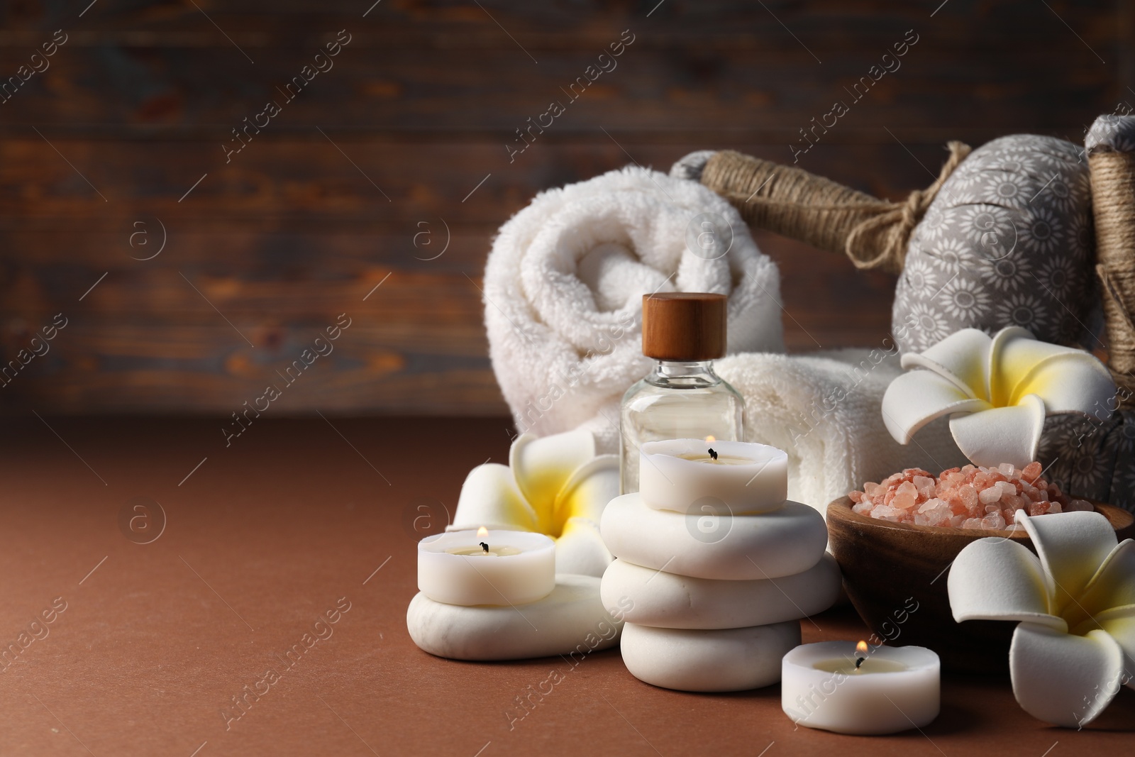 Spa composition. Massage bags, stones, towels, cosmetic products, plumeria flowers and burning candles on dark beige table, closeup. Space for text Photo of Spa composition. Massage bags, stones, towels, cosmetic products, plumeria flowers and burning candles on dark beige table, closeup. Space for text