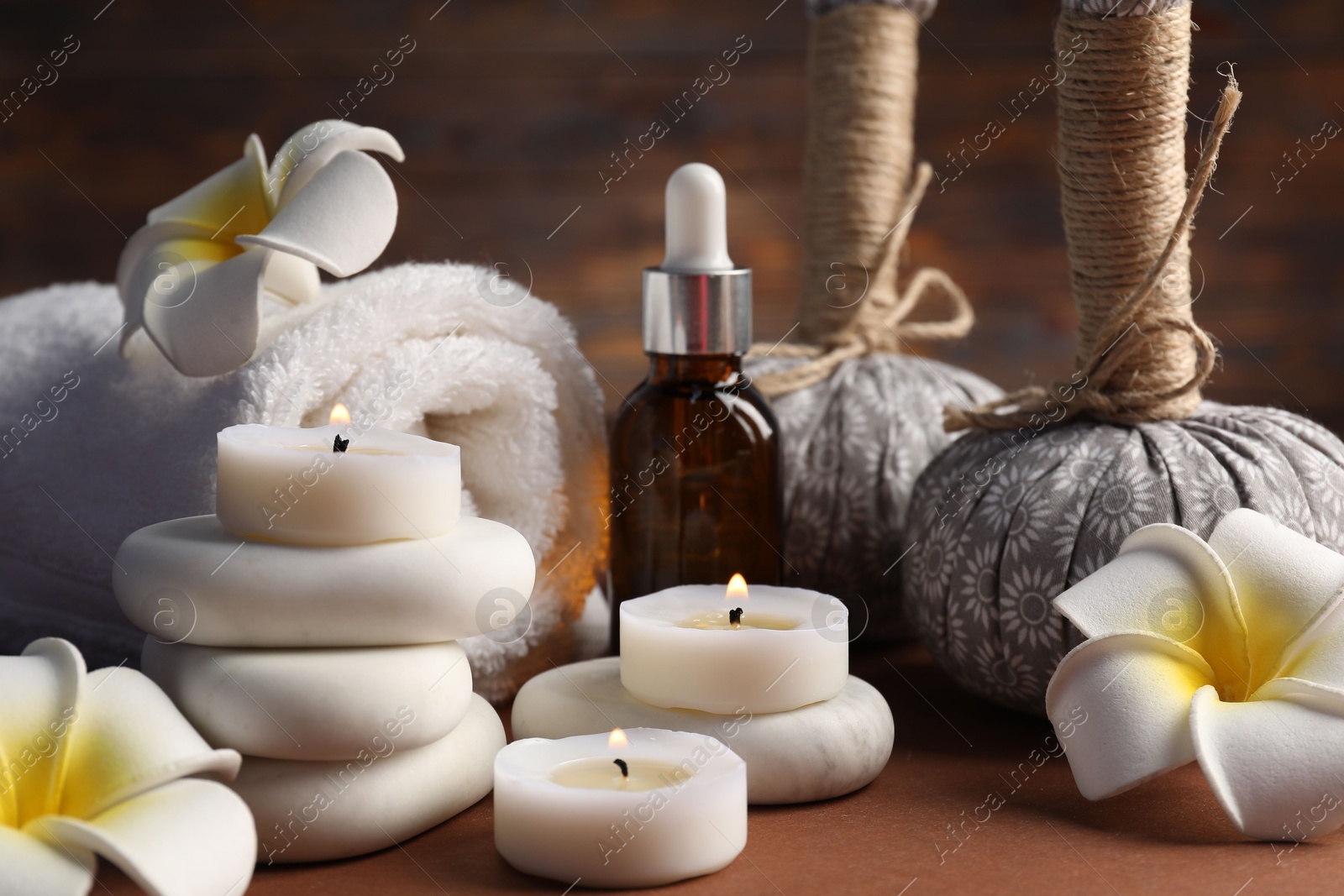Massage bags, stones, towel, cosmetic product, plumeria flowers and burning candles on dark beige table, closeup. Spa composition Photo of Massage bags, stones, towel, cosmetic product, plumeria flowers and burning candles on dark beige table, closeup. Spa composition