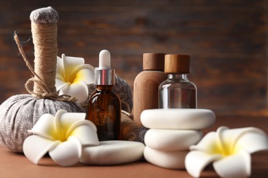 Photo of Massage bags, stones, cosmetic products and plumeria flowers on dark beige table, closeup. Spa composition