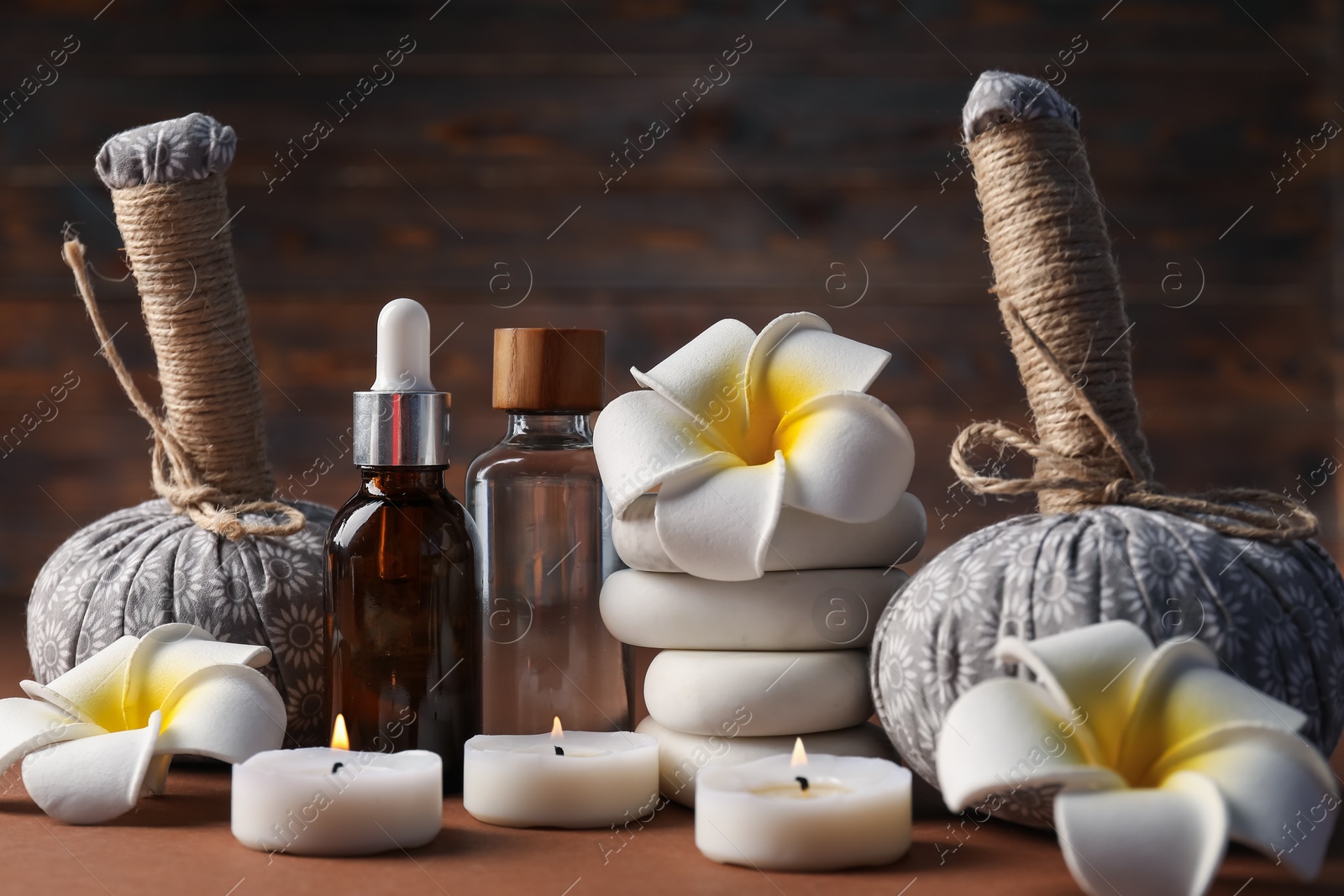 Massage bags, stones, cosmetic products, burning candles and plumeria flowers on dark beige table, closeup. Spa composition Photo of Massage bags, stones, cosmetic products, burning candles and plumeria flowers on dark beige table, closeup. Spa composition