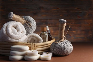 Photo of Spa composition. Massage bags, stones, towels, cosmetic products and burning candles on dark beige table, closeup. Space for text