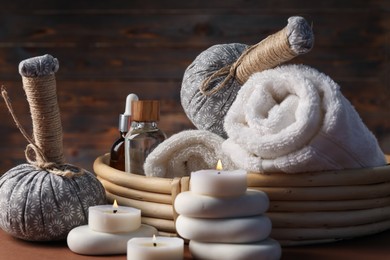 Photo of Massage bags, stones, towels, cosmetic products and burning candles on dark beige table, closeup. Spa composition