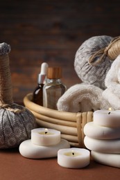 Photo of Massage bags, stones, towels, cosmetic products and burning candles on dark beige table, closeup. Spa composition
