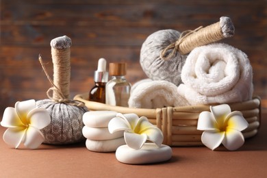 Photo of Massage bags, stones, towels, cosmetic products and plumeria flowers on dark beige table, closeup. Spa composition