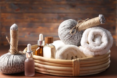 Photo of Massage bags, towels and cosmetic products on dark beige table, closeup. Spa composition