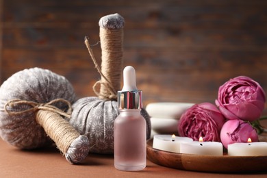 Photo of Massage bags, cosmetic product, burning candles and peony flowers on dark beige table, closeup. Spa composition