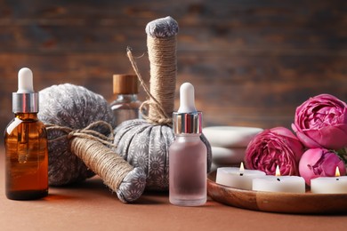 Photo of Massage bags, cosmetic products, burning candles and peony flowers on dark beige table, closeup. Spa composition