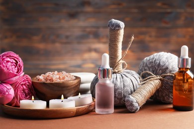 Photo of Massage bags, cosmetic products, burning candles and peony flowers on dark beige table, closeup. Spa composition