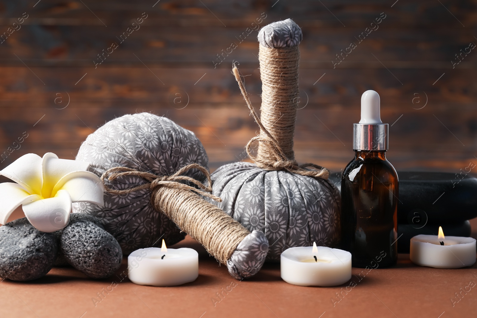 Massage bags, stones, cosmetic product, burning candles and plumeria flower on dark beige table, closeup. Spa composition Photo of Massage bags, stones, cosmetic product, burning candles and plumeria flower on dark beige table, closeup. Spa composition