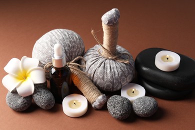 Photo of Massage bags, stones, cosmetic product, burning candles and plumeria flower on dark beige background, closeup