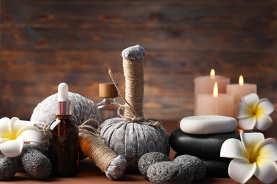 Photo of Massage bags, stones, cosmetic products, burning candles and plumeria flowers on table, closeup. Spa composition
