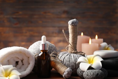 Photo of Massage bags, stones, cosmetic product, towel burning candles and plumeria flowers on table, closeup. Spa composition