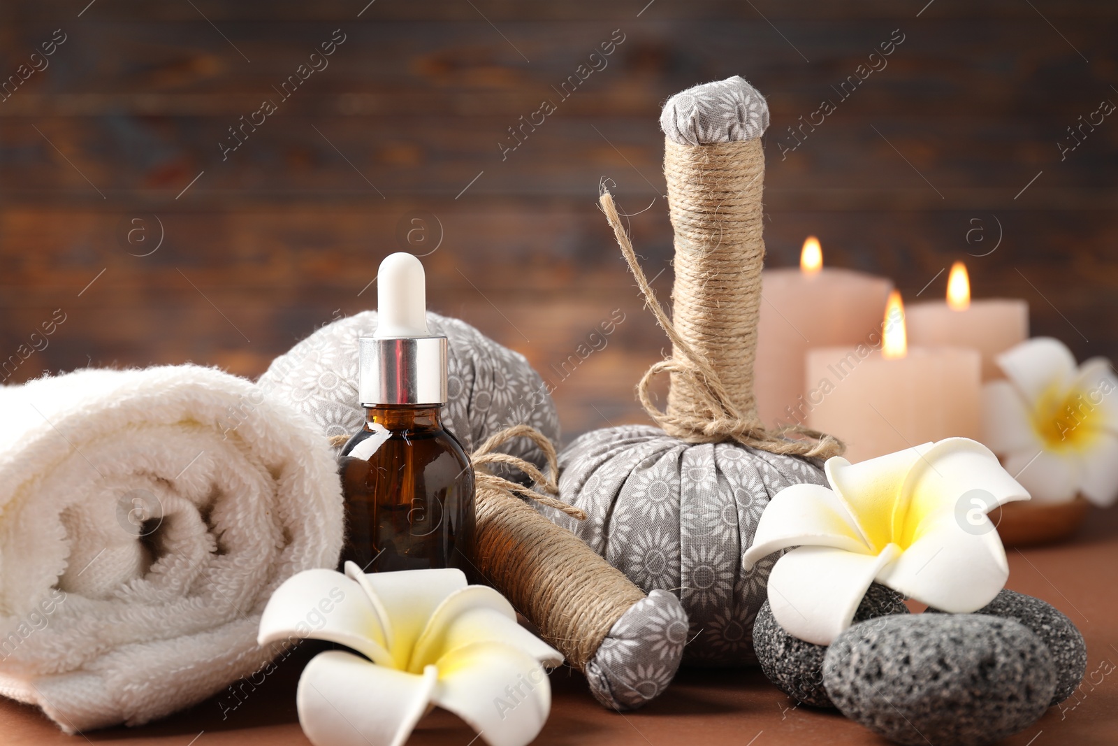 Massage bags, stones, cosmetic product, towel burning candles and plumeria flowers on dark beige table, closeup. Spa composition Photo of Massage bags, stones, cosmetic product, towel burning candles and plumeria flowers on dark beige table, closeup. Spa composition