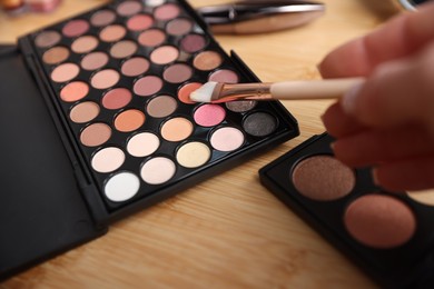 Photo of Woman with brush and eyeshadow palette at wooden vanity indoors, closeup