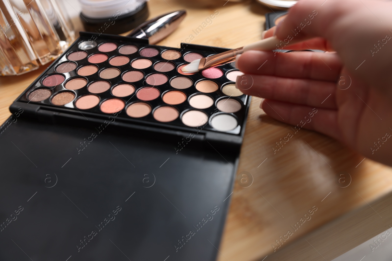Woman with brush and eyeshadow palette at wooden vanity indoors, closeup Photo of Woman with brush and eyeshadow palette at wooden vanity indoors, closeup