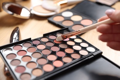 Photo of Woman with brush and eyeshadow palette at wooden vanity indoors, closeup