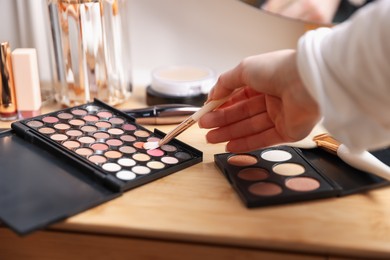 Photo of Woman with brush and eyeshadow palette at wooden vanity indoors, closeup