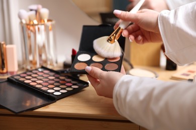 Photo of Woman with brush and eyeshadow palette at wooden vanity indoors, closeup