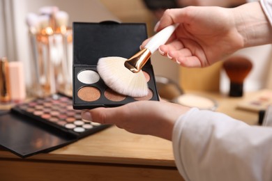 Photo of Woman with brush and eyeshadow palette at wooden vanity indoors, closeup