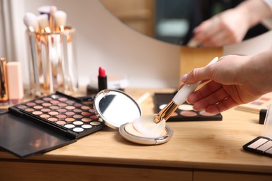 Photo of Woman with brush and eyeshadow palette at wooden vanity indoors, closeup