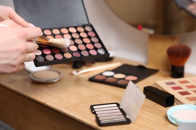 Photo of Woman with brush and eyeshadow palette at wooden vanity indoors, closeup