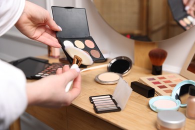 Photo of Woman with brush and eyeshadow palette at wooden vanity indoors, closeup