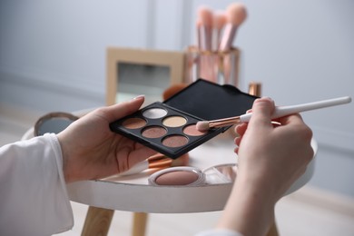 Photo of Woman with brush and eyeshadow palette at table indoors, closeup