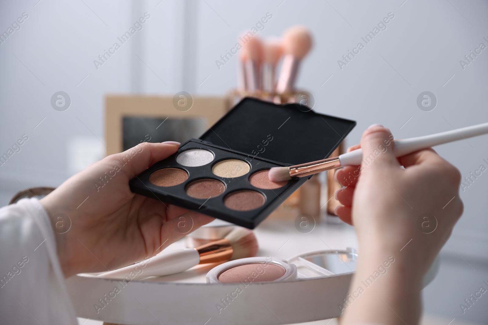 Woman with brush and eyeshadow palette at table indoors, closeup Photo of Woman with brush and eyeshadow palette at table indoors, closeup