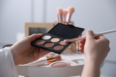 Photo of Woman with brush and eyeshadow palette at table indoors, closeup
