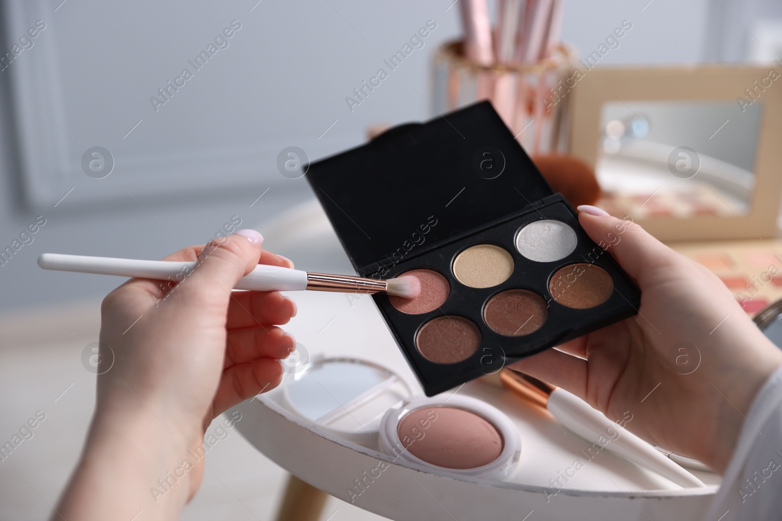 Woman with brush and eyeshadow palette at table indoors, closeup Photo of Woman with brush and eyeshadow palette at table indoors, closeup