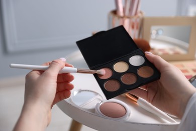 Photo of Woman with brush and eyeshadow palette at table indoors, closeup